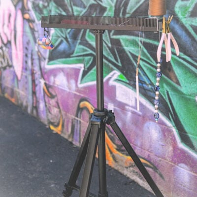 Hair Butler™ hair extension workstation tool sits on tripod in front of colorful wall