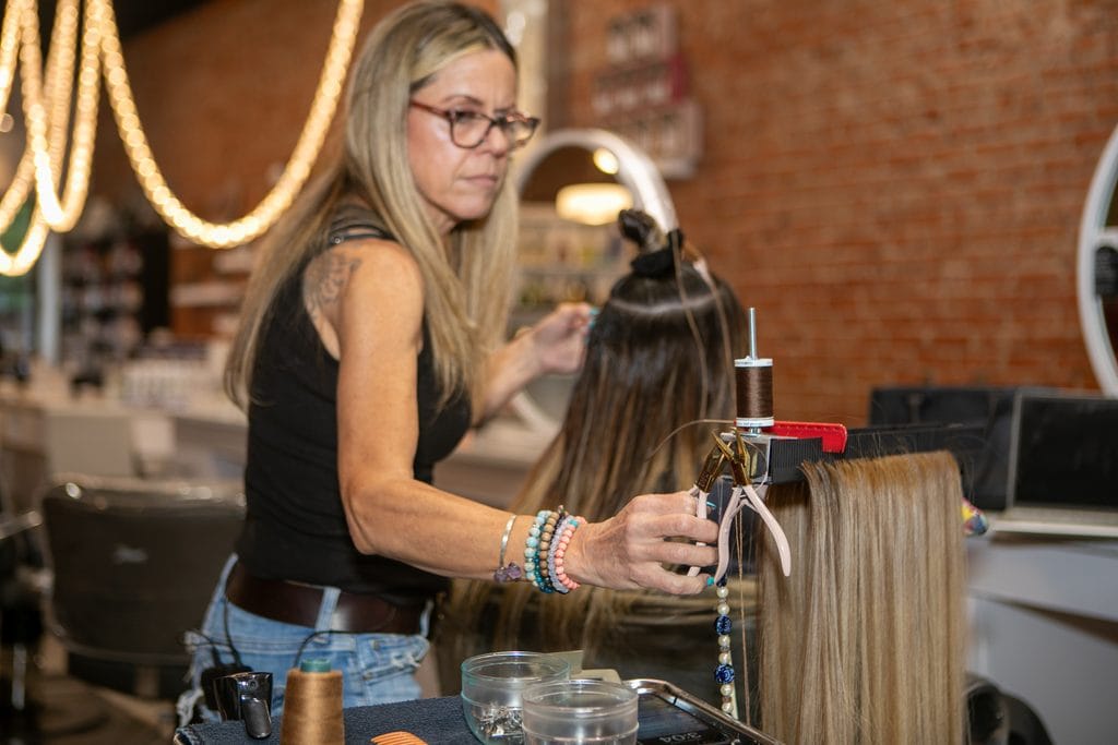Professional hair extension setup with Hair Butler holding extension hair and tools while a stylist works on a client.