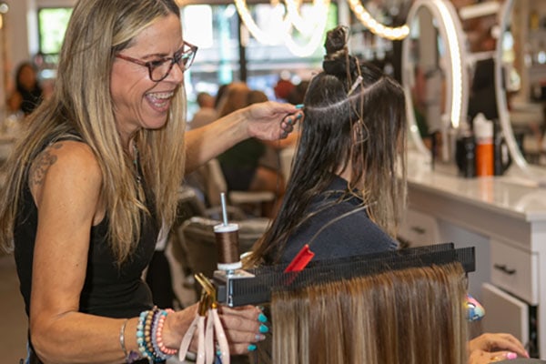 close up of Laura smiling while adding extensions to client using Hair Butler™ hair extension workstation tool in salon