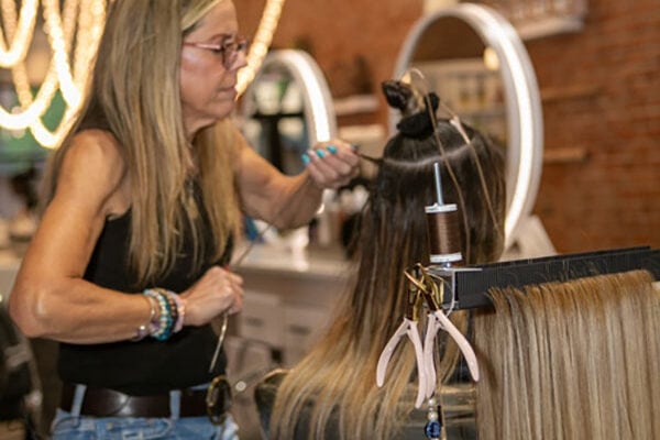 professional stylist adds hair extensions to client's hair using Hair Butler™ hair extension workstation tool